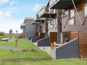 A row of modern, multi-story buildings with balconies, a grassy area, and a paved walkway. - 4 Star Holiday Home in Bogense (Bogense)