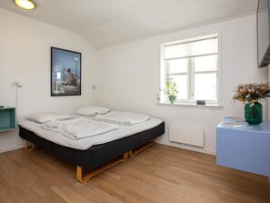Een slaapkamer met een bed, een raam met uitzicht, een nachtkastje en een poster aan de muur.