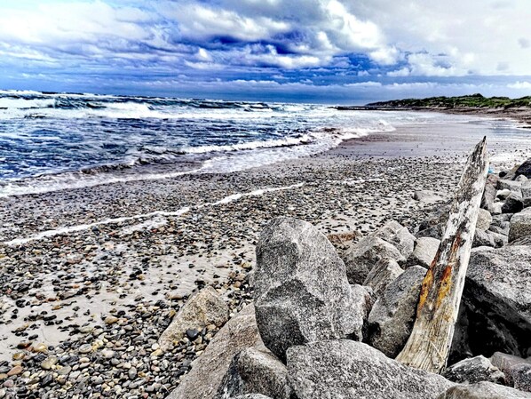 A rocky beach with waves, a wooden post, and a cloudy sky.