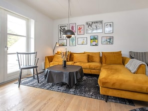 Un salon avec un canapé, une table et une chaise. Les murs sont ornés de tableaux encadrés et il y a une fenêtre d’où l’on peut profiter de la vue.
