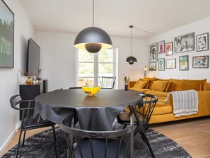 A modern living room with a round dining table, black chairs, a yellow sofa, and black pendant lights.