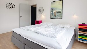 Une chambre moderne avec un grand lit, une table de chevet, une œuvre d’art accrochée au mur et une porte donnant sur une autre pièce.