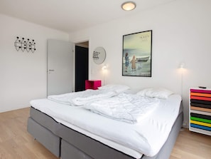 Une chambre moderne avec un grand lit, une table de chevet, une œuvre d’art accrochée au mur et une porte donnant sur une autre pièce.