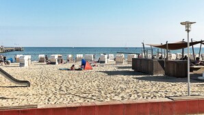 A beach with sun loungers, a lifeguard tower, and a pier in the background. - Holiday Home in Grossenbrode (Grossenbrode)