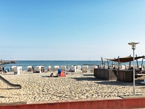 A beach with sun loungers, a lifeguard tower, and a pier in the background.