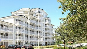 A multi-story building with balconies, a paved driveway, and parked cars. - Holiday Home in Grossenbrode (Grossenbrode)