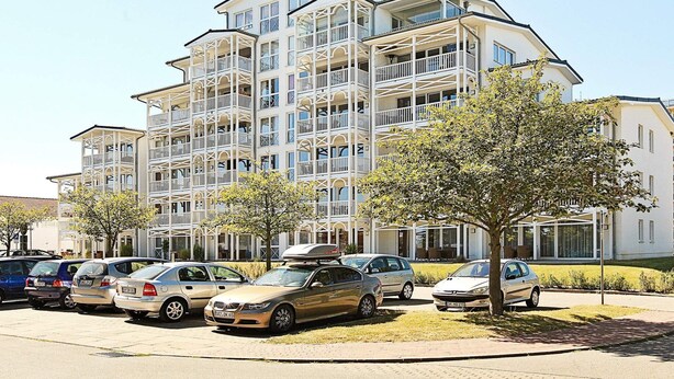 A multi-story residential building with balconies, parked cars, and trees. - Holiday Home in Grossenbrode (Grossenbrode)
