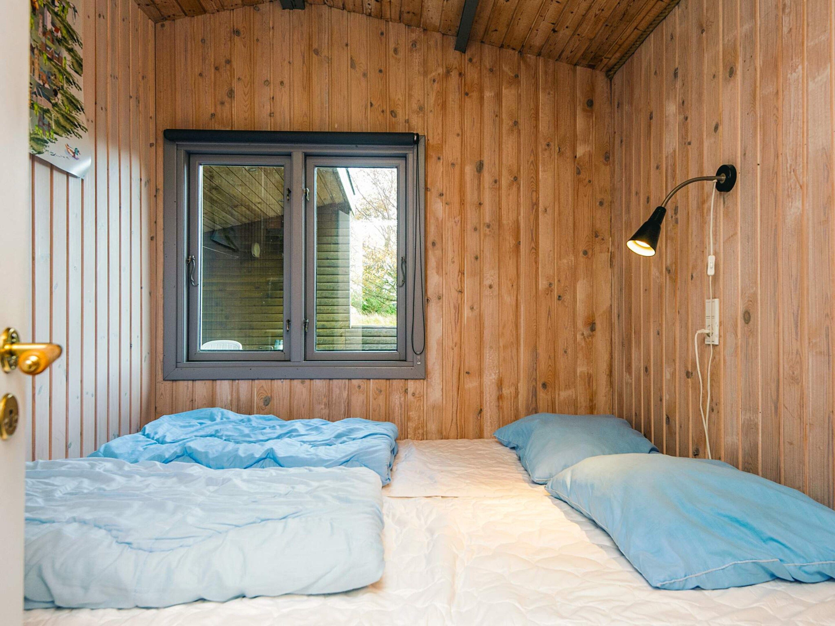 Een kamer met houten wanden, een raam met zonwering, twee bedden met blauw beddengoed en een enkele bedlamp.