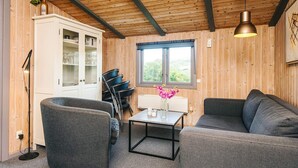Ett mysigt rum med ett träpanelat tak, en soffa, en fåtölj, ett bord med en vas med blommor och ett skåp med glasdörrar.