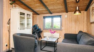 Una habitación acogedora con techo de madera, un sofá, una silla, una mesa con un jarrón de flores y un aparador con puertas de cristal.