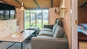 En mysig stuga med en soffa, ett bord, en tv och ett fönster med utsikt över naturen.