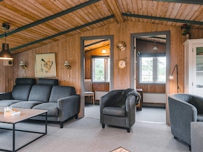 A cozy interior with a wooden ceiling, grey upholstered seating, a coffee table, and a view through a doorway to an outdoor area.