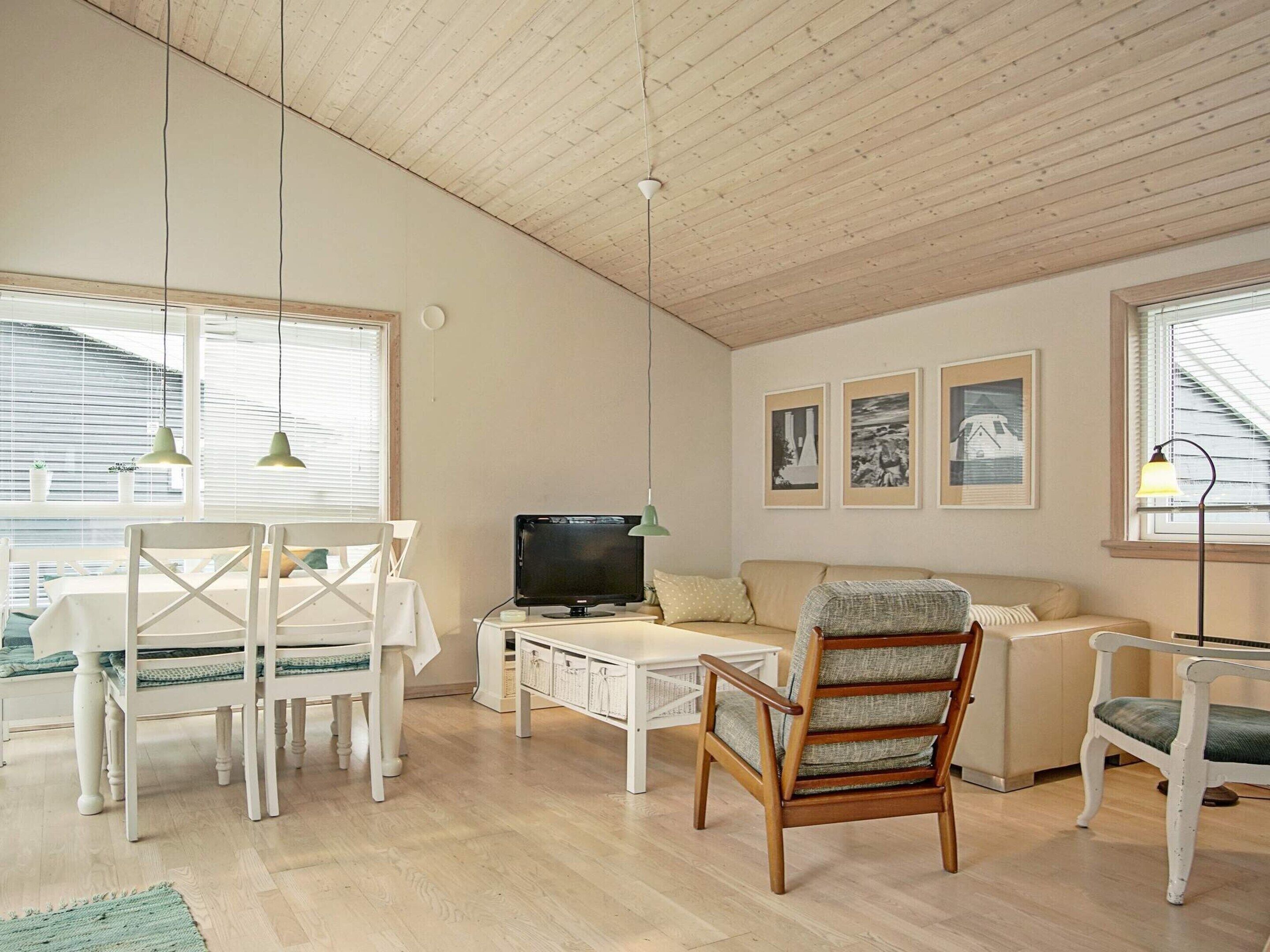 A living room with a wooden ceiling, a television, a sofa, a dining table with chairs, and framed pictures on the wall.