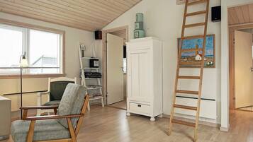 A room with a wooden floor, a chair, a white cabinet, a ladder, and a painting on the wall.