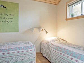 Une chambre avec deux lits, une étagère fixée au mur, une lampe de bureau et une fenêtre donnant sur des arbres.