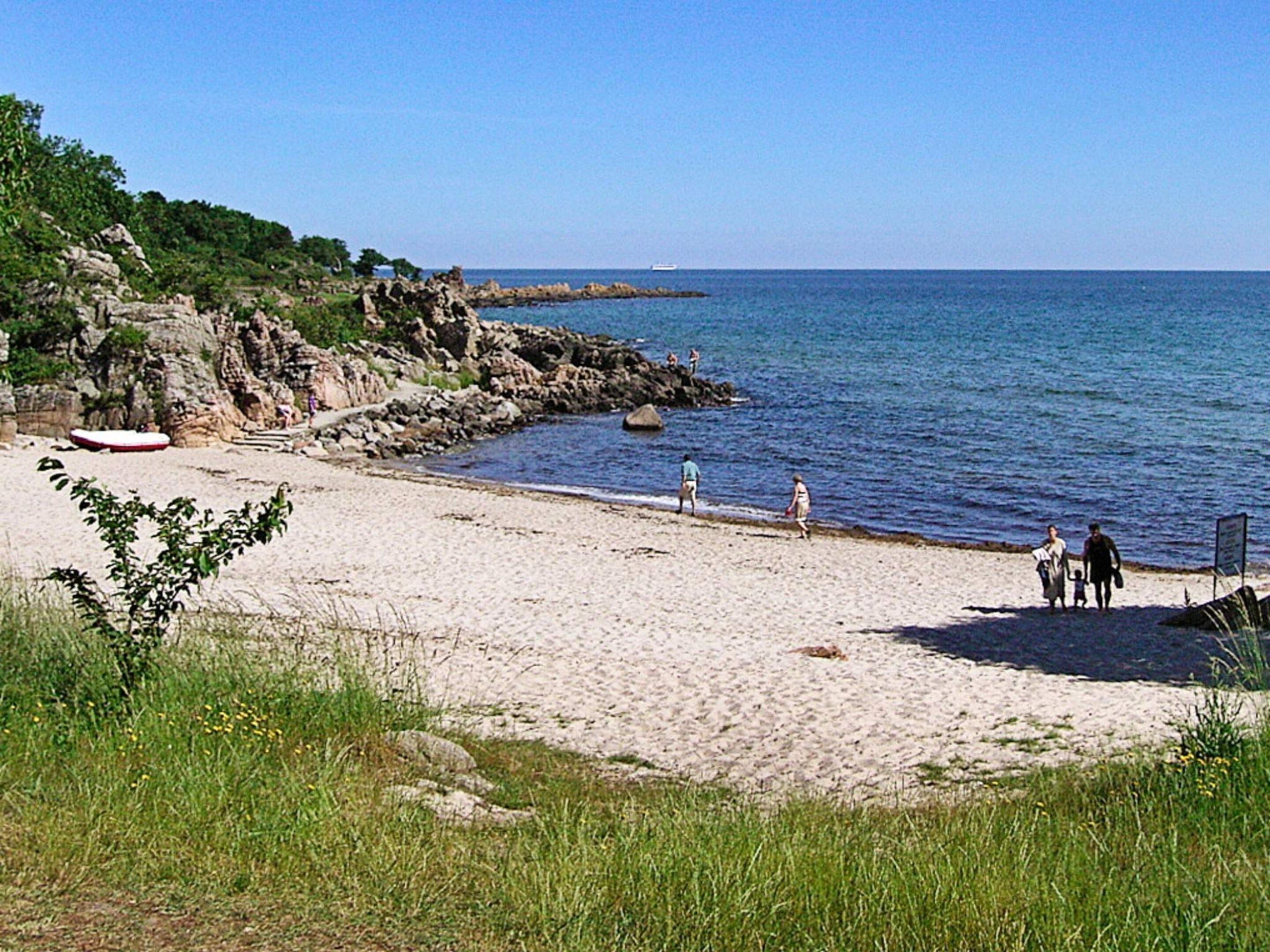 A beach with rocky cliffs, a sandy shore, and calm sea.