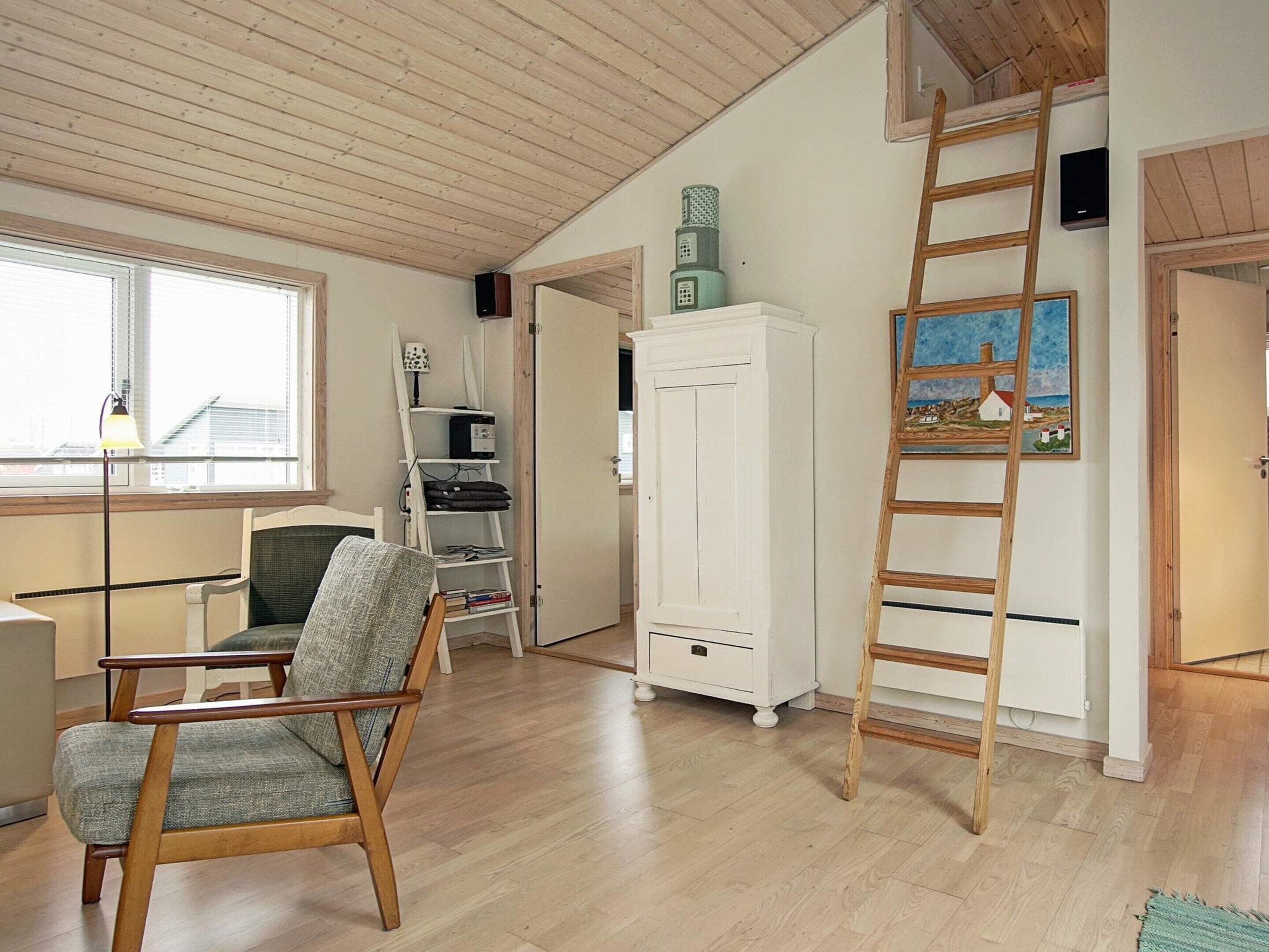 A room with a wooden floor, a white cabinet, a chair, a ladder, and a painting on the wall.