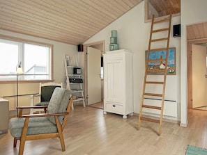 A room with a wooden floor, a white cabinet, a chair, a ladder, and a painting on the wall.