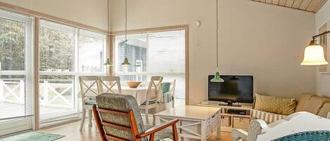 A modern living room with a wooden ceiling, a television, and a dining area with chairs and a table.