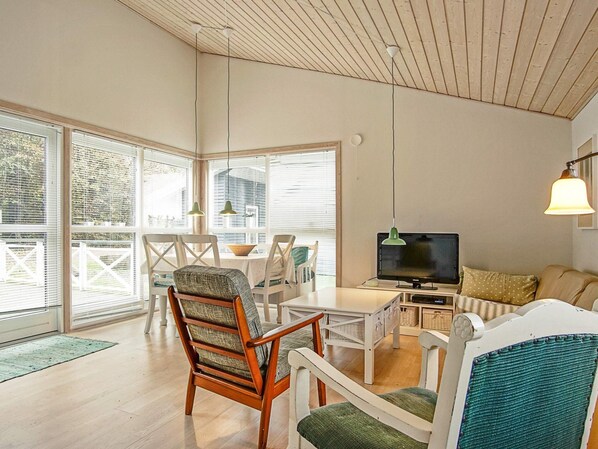 A modern living room with a wooden ceiling, a television, and a dining area with chairs and a table.