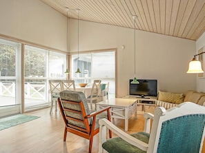 A modern living room with a wooden ceiling, a television, and a dining area with chairs and a table.