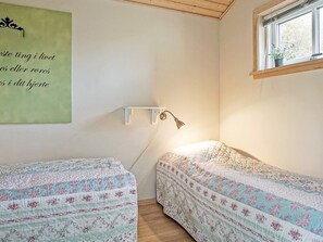 A bedroom with two single beds, a bedside lamp, a green wall with text, and a window with a plant. - 4 Person Holiday Home in Gudhjem (Gudhjem)