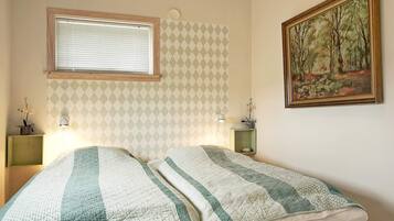 A bedroom with two beds, a window, a painting, and a patterned wall.