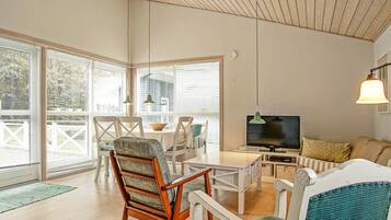 A spacious living area with a wooden ceiling, a television, and a dining table with chairs.