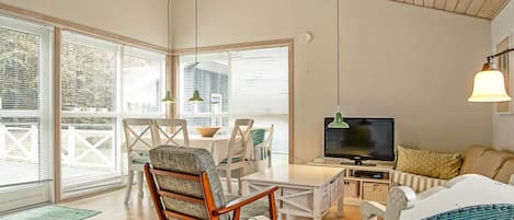 A spacious living area with a wooden ceiling, a television, and a dining table with chairs.