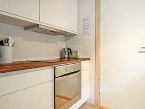 A compact kitchen with white cabinetry, a stainless steel kettle, and a built-in oven.