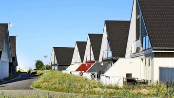 A row of modern houses with sloped roofs, a paved road, and a grassy area in the foreground.