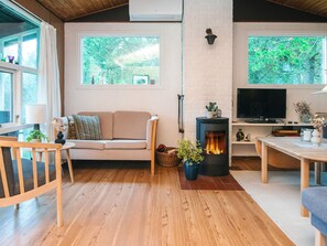 A cozy living room with a sofa, a table, a fireplace, and large windows.