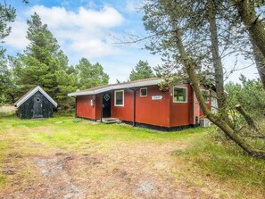 A red cabin with a small porch and a door, surrounded by trees and a grassy area.