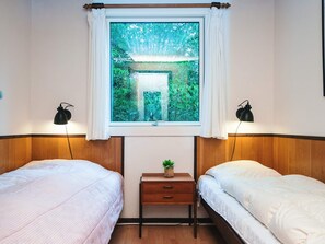 A bedroom with two beds, a window with a view of greenery, and two bedside lamps.
