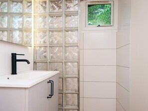 Une salle de bain avec un lavabo blanc, un robinet noir et une fenêtre donnant sur un paysage verdoyant.