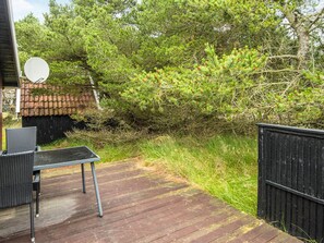 Une terrasse en bois avec une chaise et une antenne parabolique, entourée d’une végétation luxuriante et d’une clôture noire.
