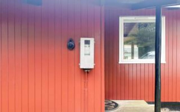 A red building with a window and a small electrical box on the wall.
