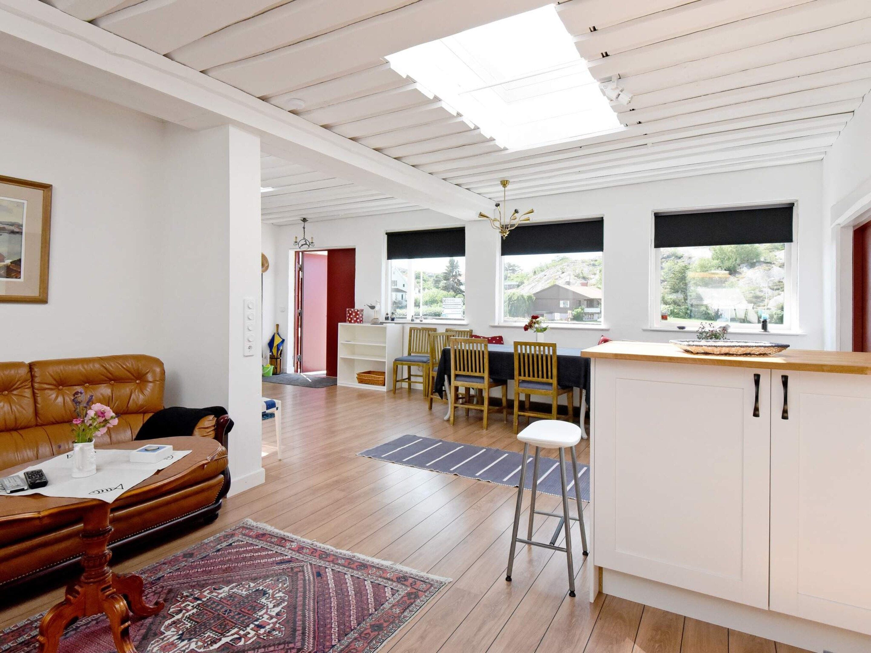 Un grand espace de vie comprenant un canapé, une table à manger avec des chaises, un coin cuisine avec un comptoir, et une vue dégagée grâce à de grandes fenêtres.