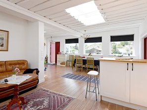 Un espacio habitable amplio con un sofá, una mesa de comedor con sillas, una zona de cocina con mostrador y vistas a través de amplias ventanas.