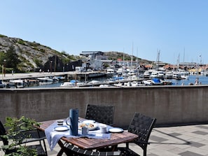 Une table à manger avec des assiettes, un pichet et une tasse, donnant sur une marina où l’on peut voir des bateaux et des bâtiments.