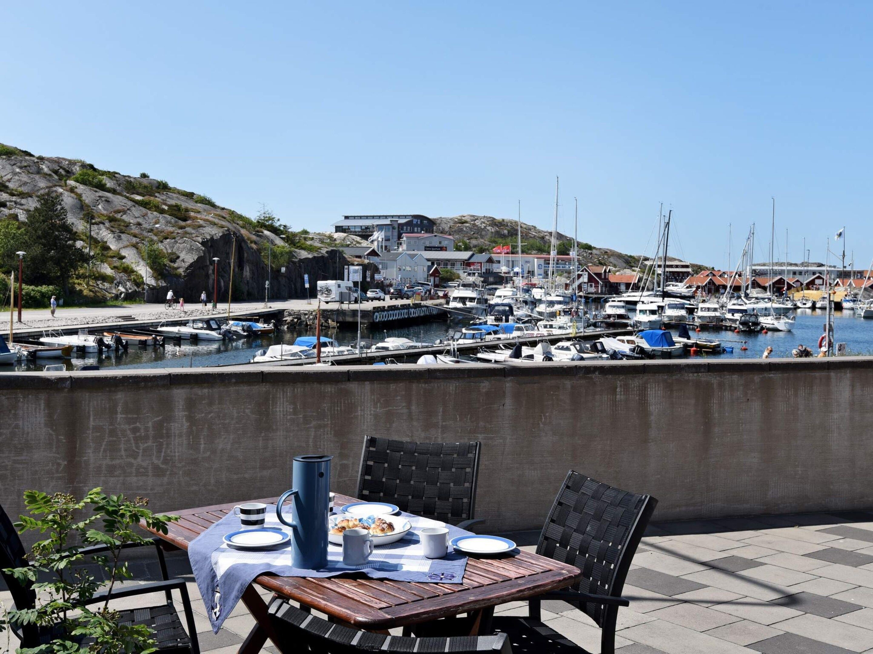 A dining table with plates, a pitcher, and a mug set outdoors with a view of a marina and boats.