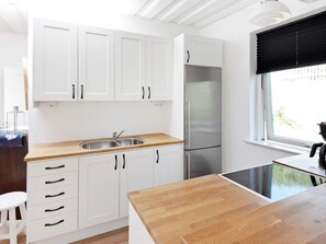 Une cuisine avec des meubles blancs, un réfrigérateur en acier inoxydable, un plan de travail en bois et une fenêtre donnant sur un beau paysage.
