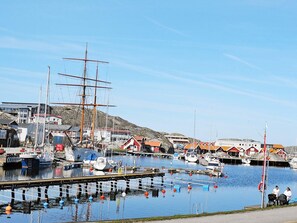 Un port où sont amarrés divers bateaux, dont un grand voilier, le long de bâtiments aux toits rouges.