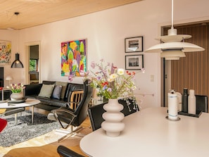 A modern living room with a black leather sofa, a white dining table with a vase of flowers, and a colorful abstract painting on the wall.