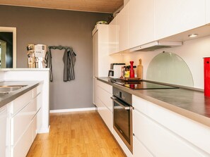 Eine moderne Küche mit weißen Schränken, einer Edelstahl-Spüle, einem Holzboden und einem roten Behälter auf der Arbeitsfläche.