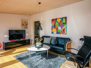 A modern living room with a black leather sofa, a glass coffee table, and a colorful abstract painting on the wall.
