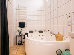 Ett modernt badrum med ett fristående badkar, ett litet bord med toalettartiklar och ett fönster med persienner.