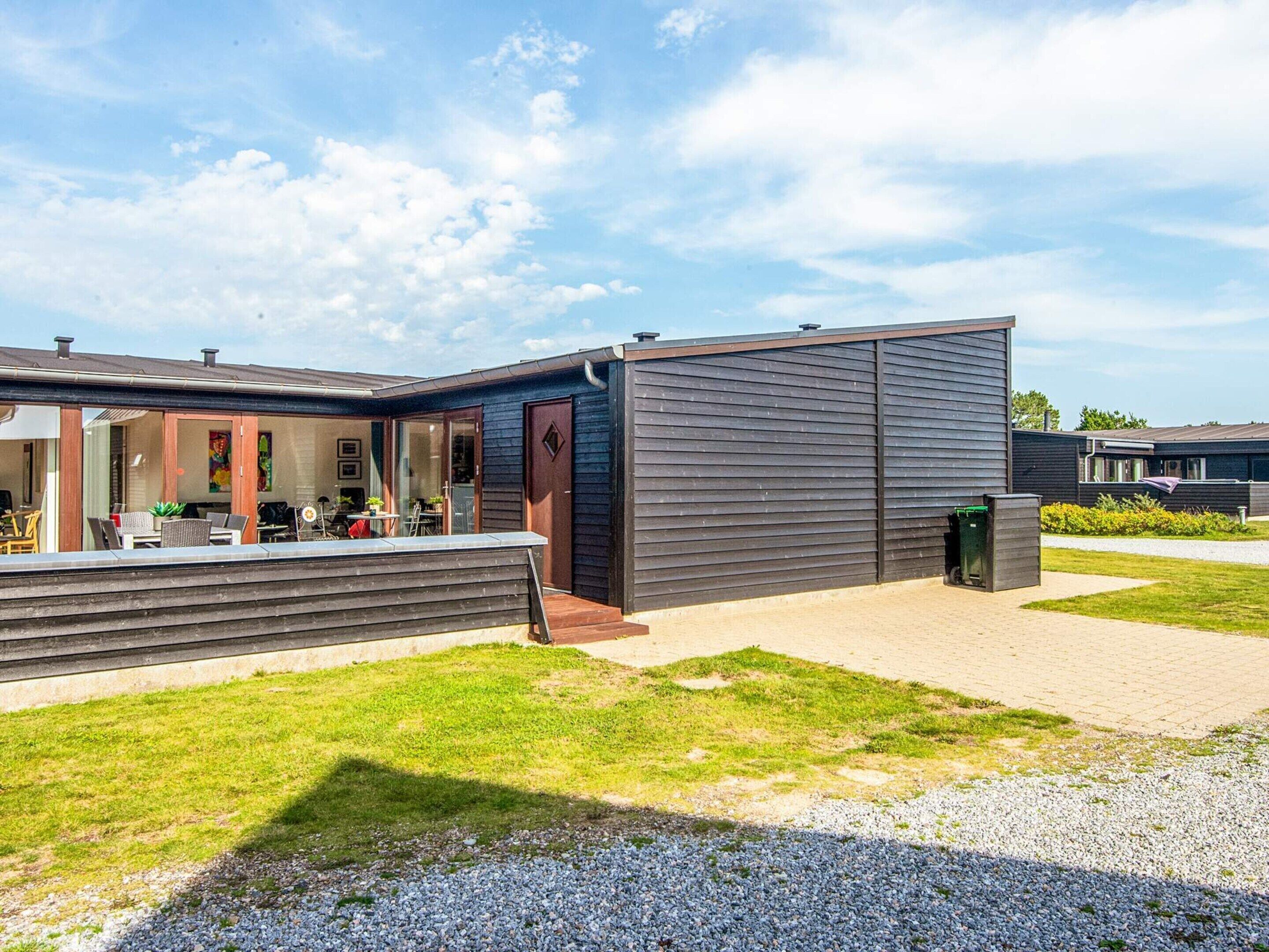 A modern building with a flat roof, a covered outdoor seating area, and a gravel pathway.