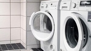 A front-loading washing machine and dryer side by side in a laundry room with tiled walls and a tiled floor. - Holiday Home in Lysekil (Lysekil)