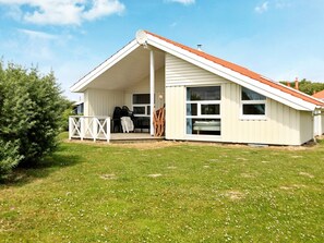 Une maison de plain-pied avec un toit en pente, une véranda et une grande fenêtre.